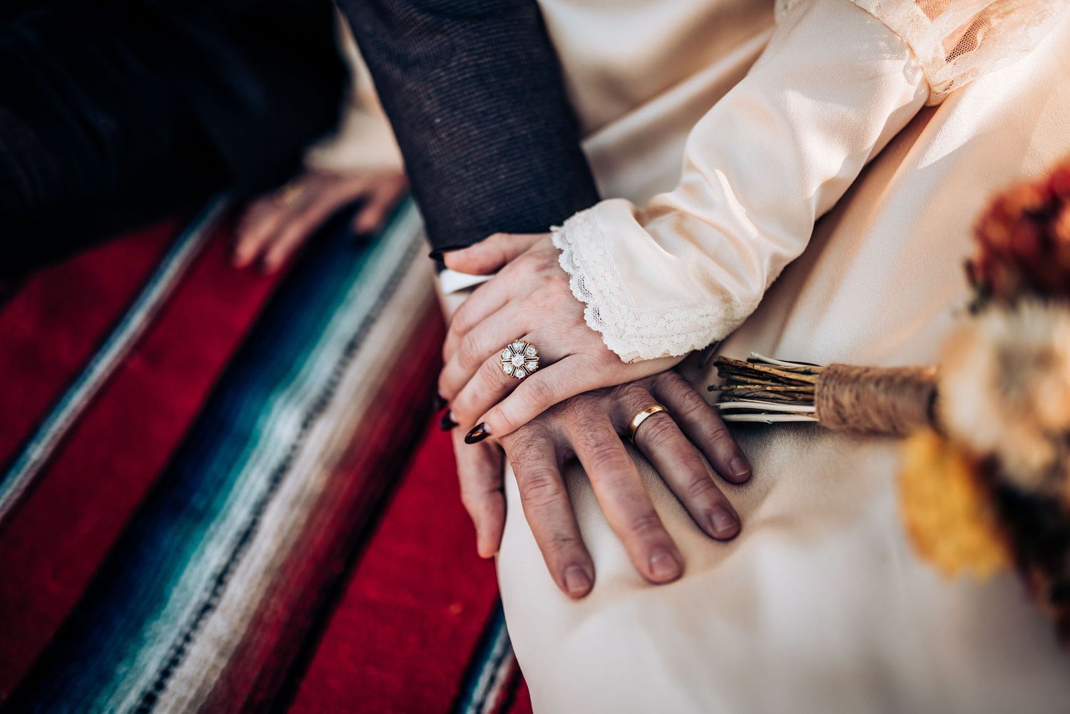 Close-up of hands showing wedding rings on a colorful striped blanket.