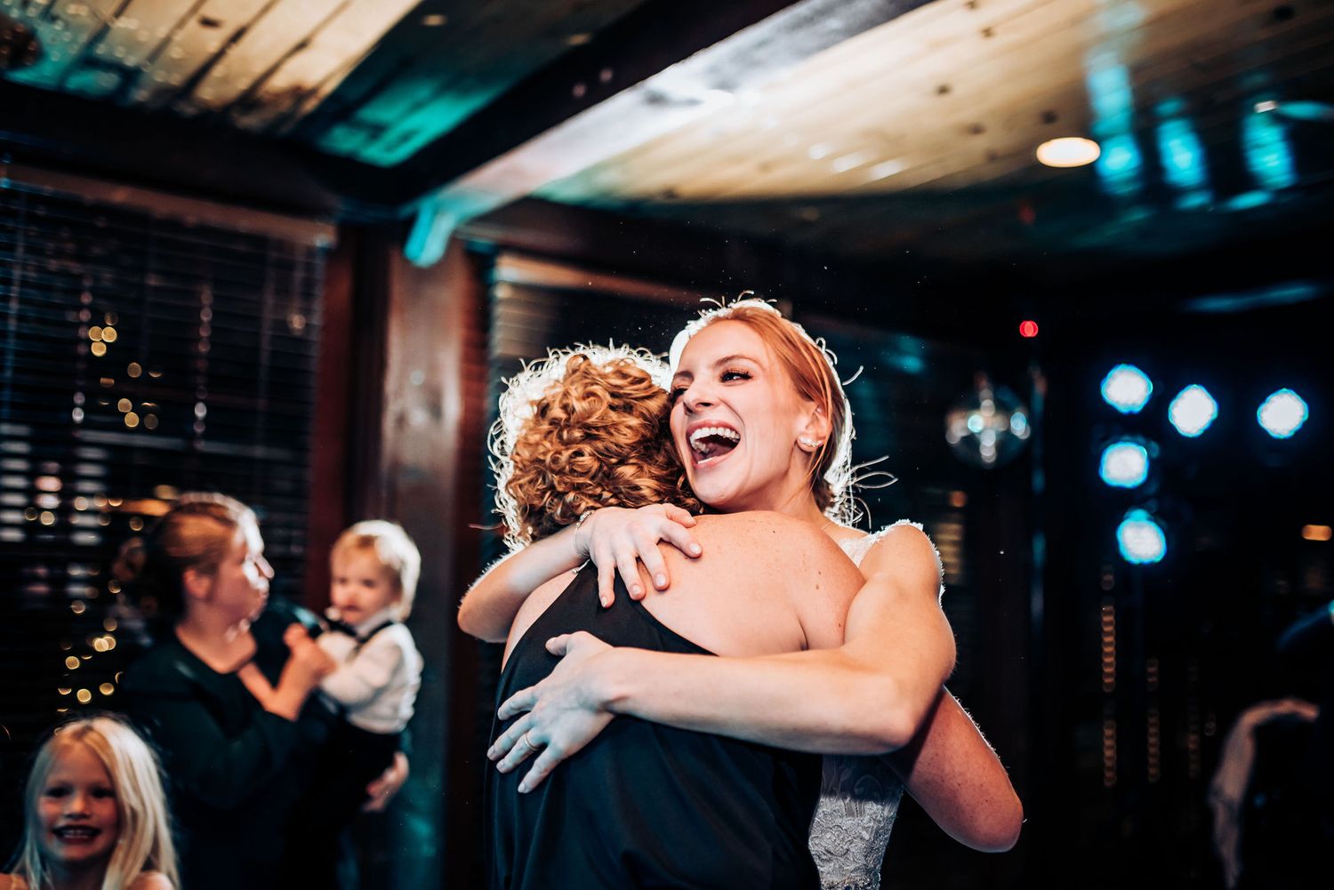 Two people share a joyful dance embrace on a dimly lit dance floor with blue lighting and festive atmosphere.