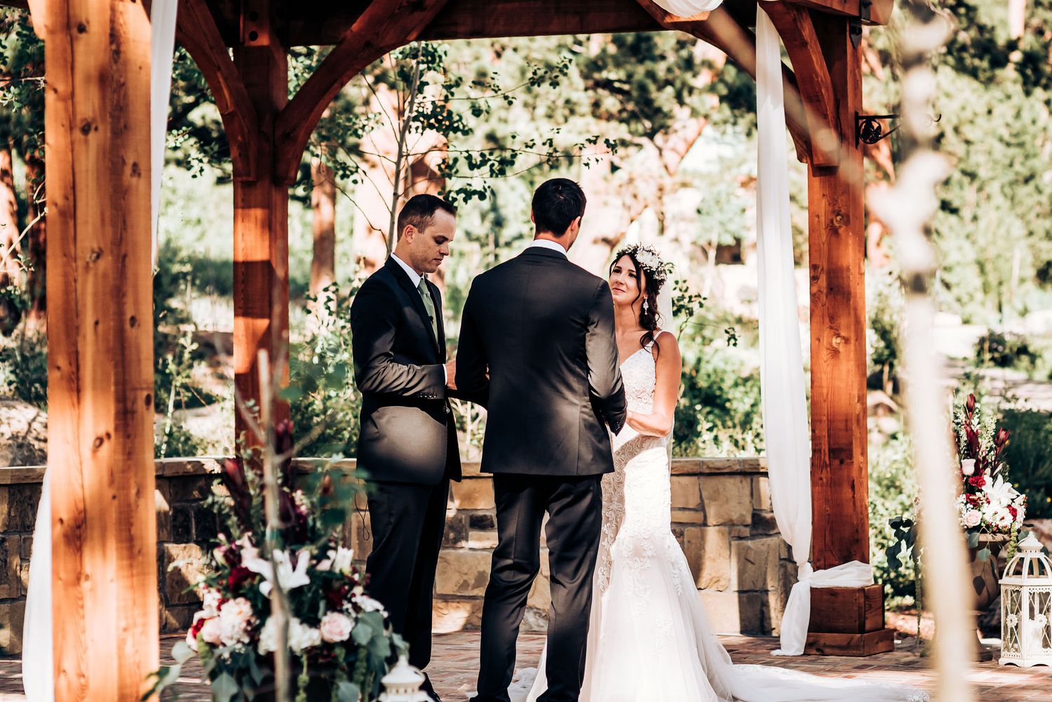 Beautiful outdoor wedding ceremony under a wooden pergola surrounded by nature.