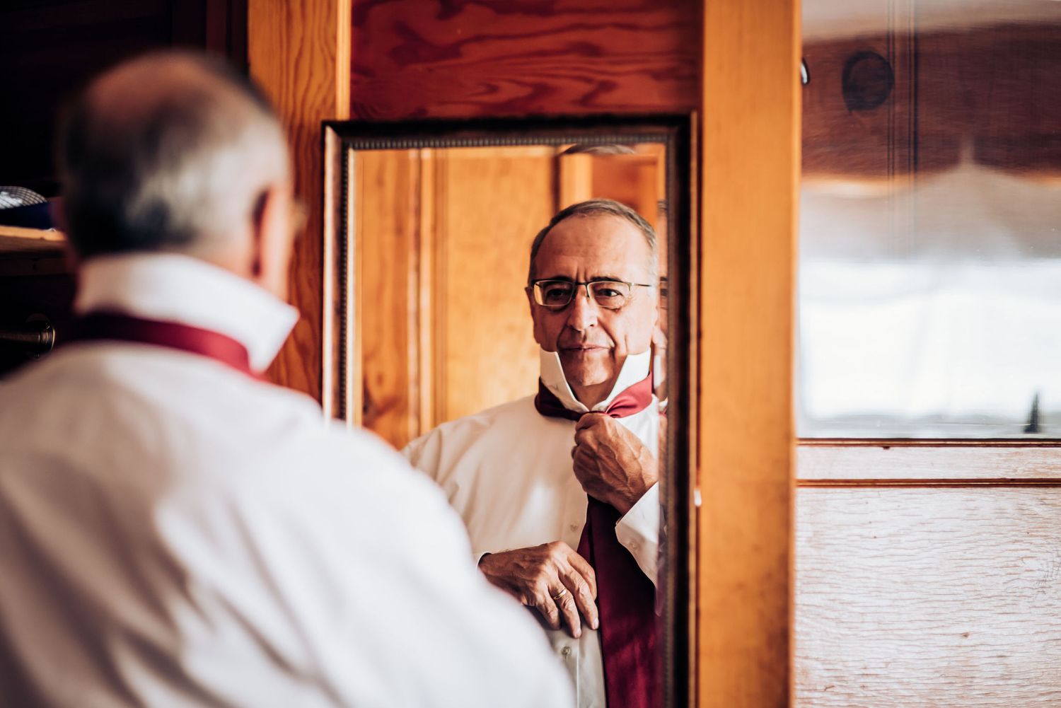 Person adjusting bow tie while looking in mirror reflection.