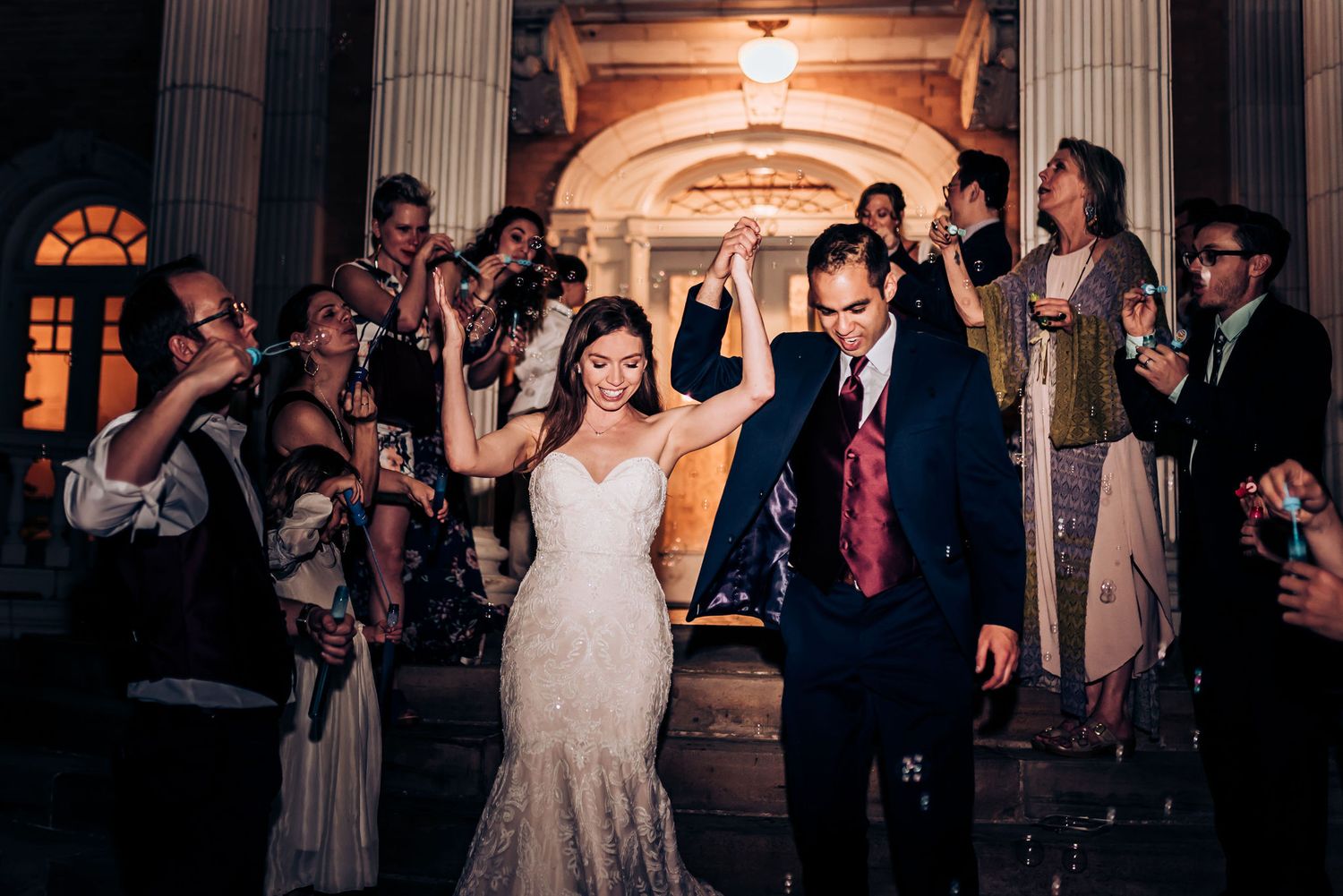 Wedding party exits through ornate columns as guests wave sparklers in celebration.