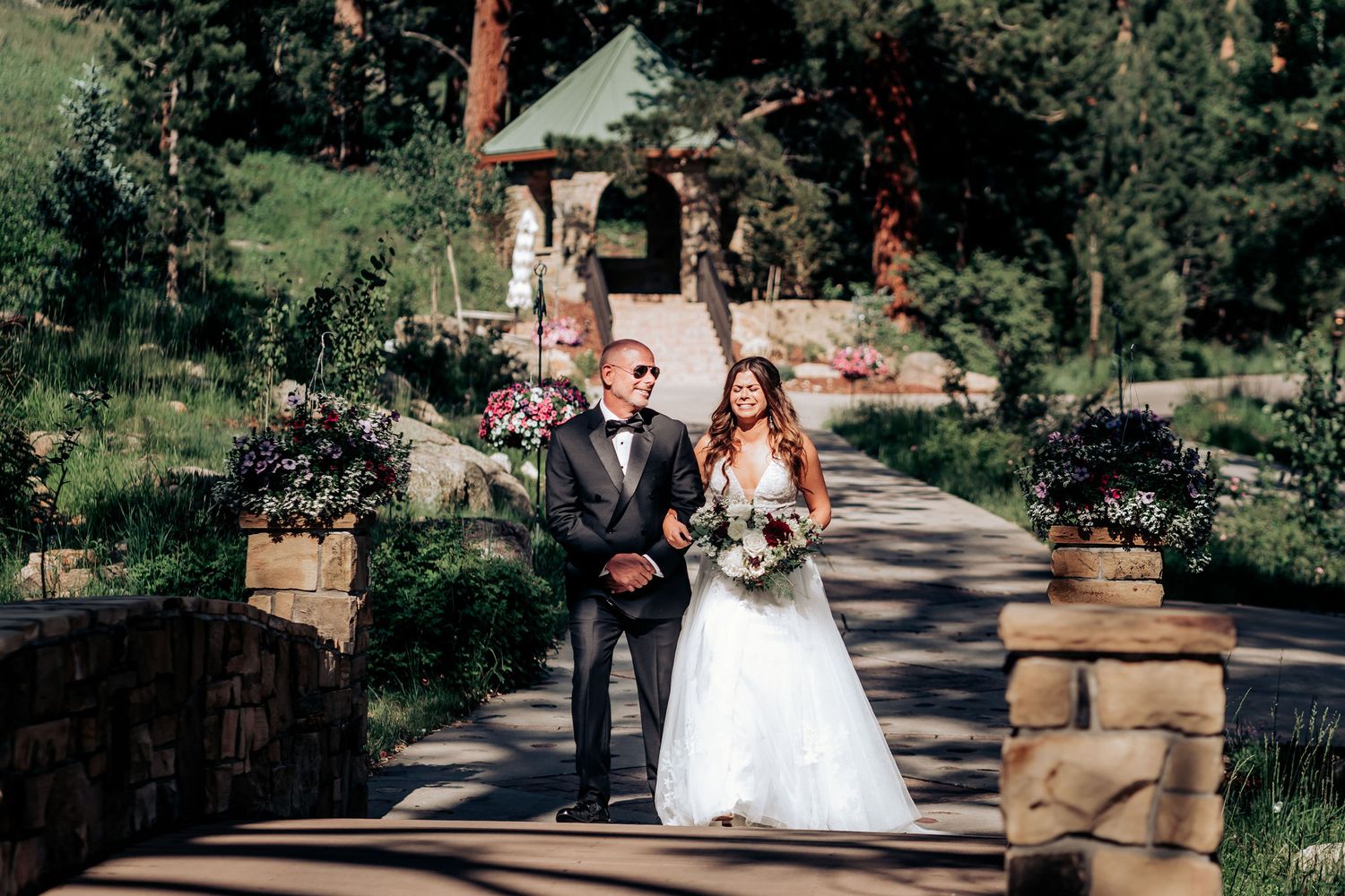 A wedding couple poses on a stone bridge with a charming gazebo in the background.
