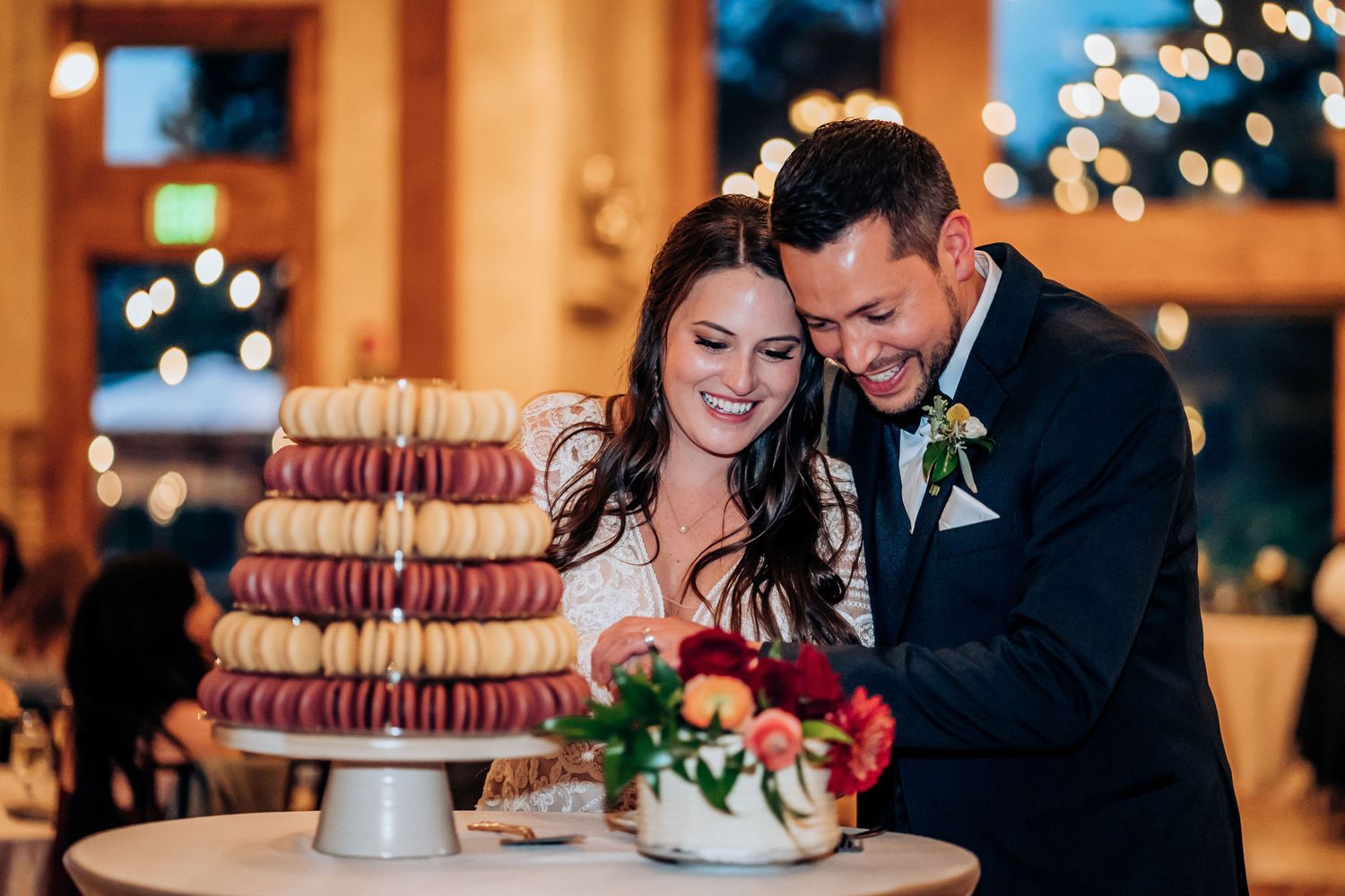 A couple shares a joyful moment while cutting their wedding cake together at an evening reception.
