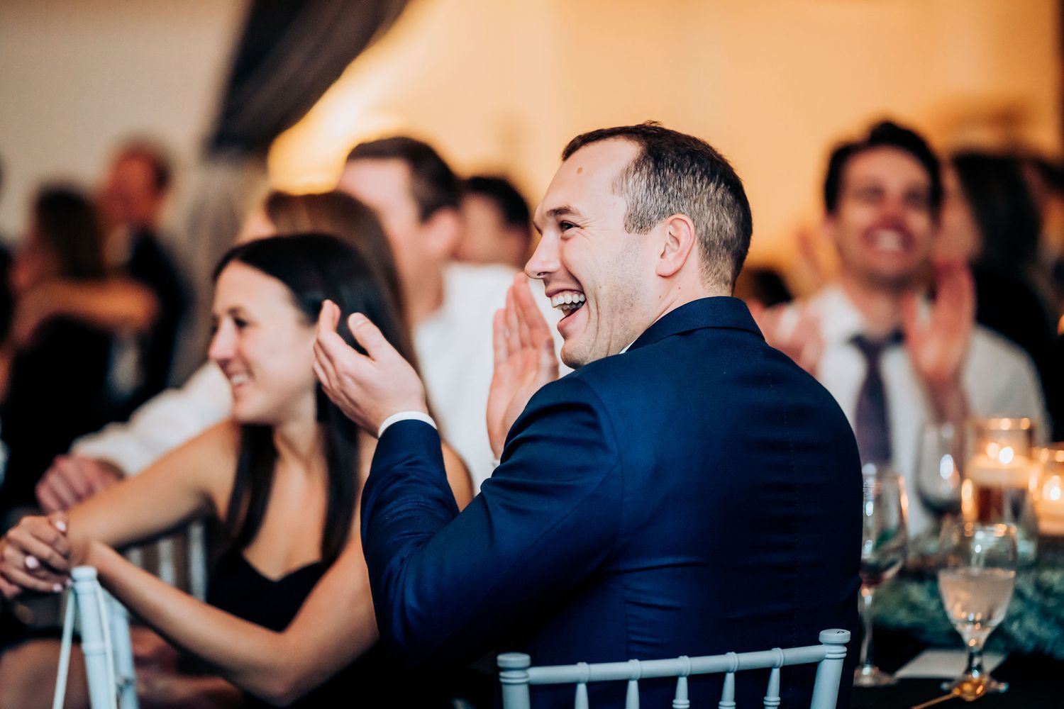 Guests react with laughter during speeches at an elegant wedding reception.