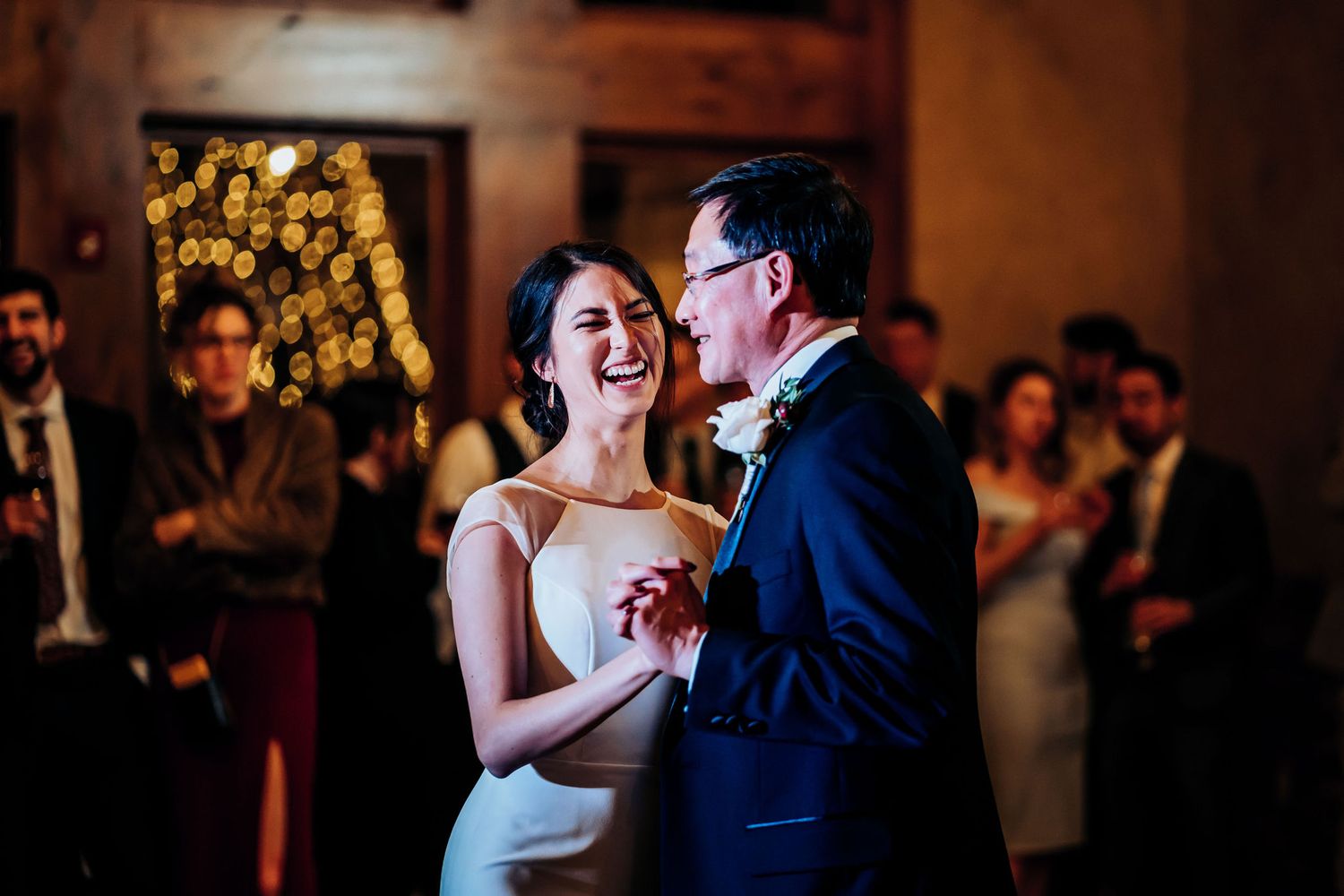 Father daughter dance surrounded by guests in an elegant ballroom with wooden floors.