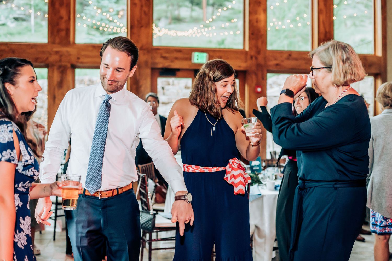 Party guests in formal attire share drinks and conversation during an indoor celebration.