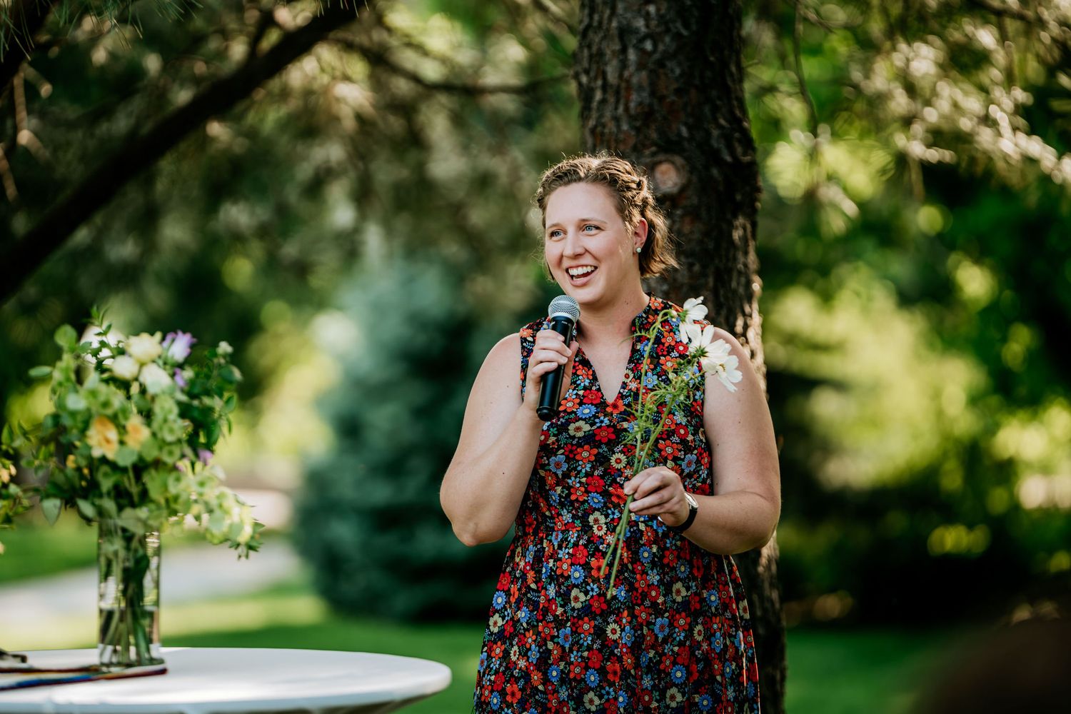 A person in a floral dress speaks at an outdoor garden event.