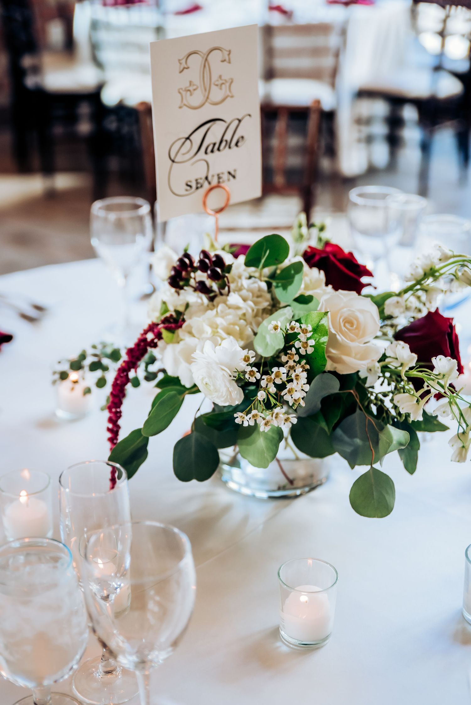 Romantic table centerpiece with burgundy and white flowers, eucalyptus leaves and vintage table number.