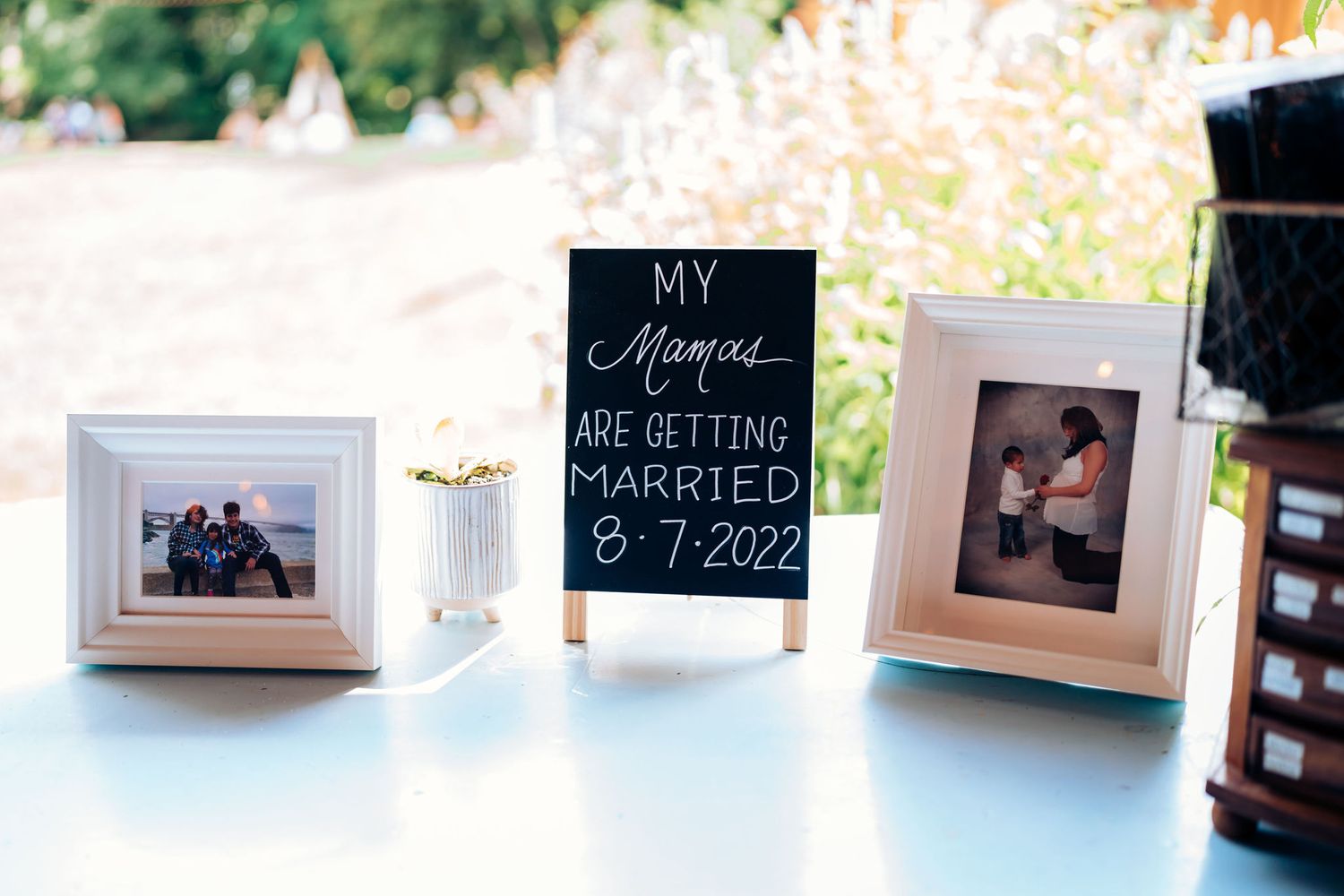 Wedding announcement display with framed photos and a chalkboard sign on white table.