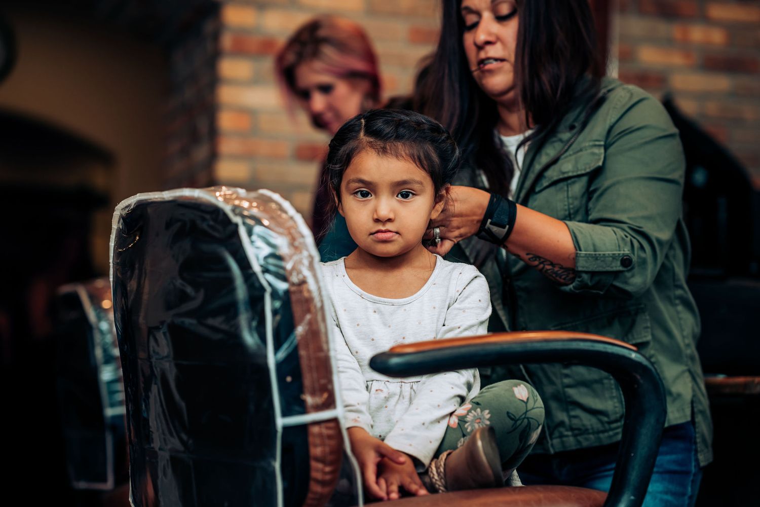Young child getting styled at a hair salon while sitting in a barber chair.