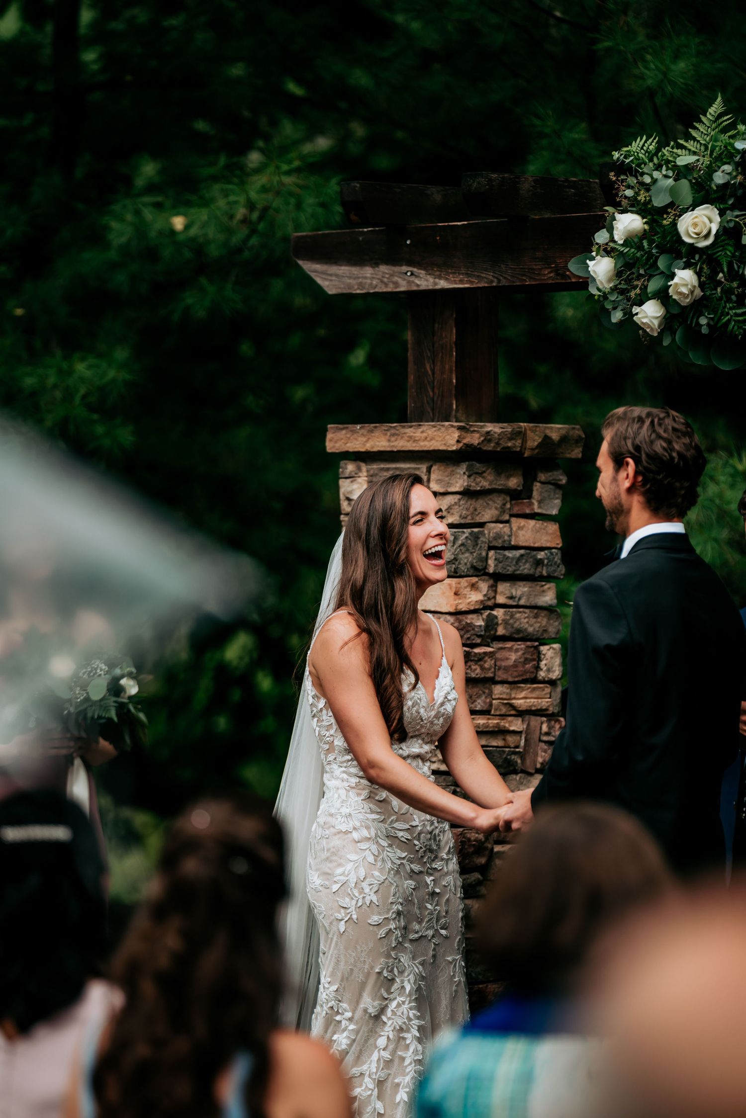 A joyful moment during an outdoor wedding ceremony with stone pillars and floral decorations.