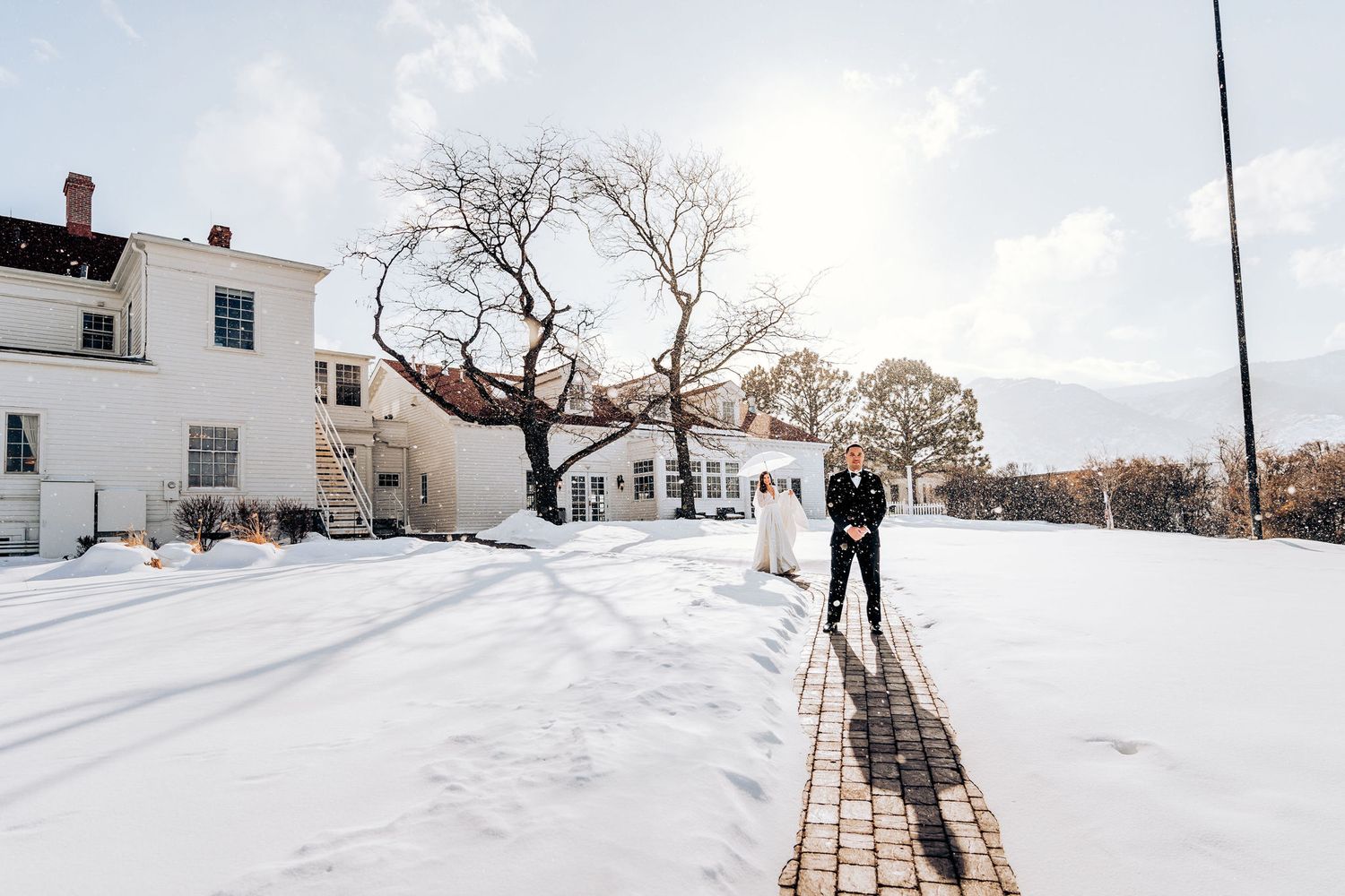 Winter wedding portrait on a snowy path with white building in background.