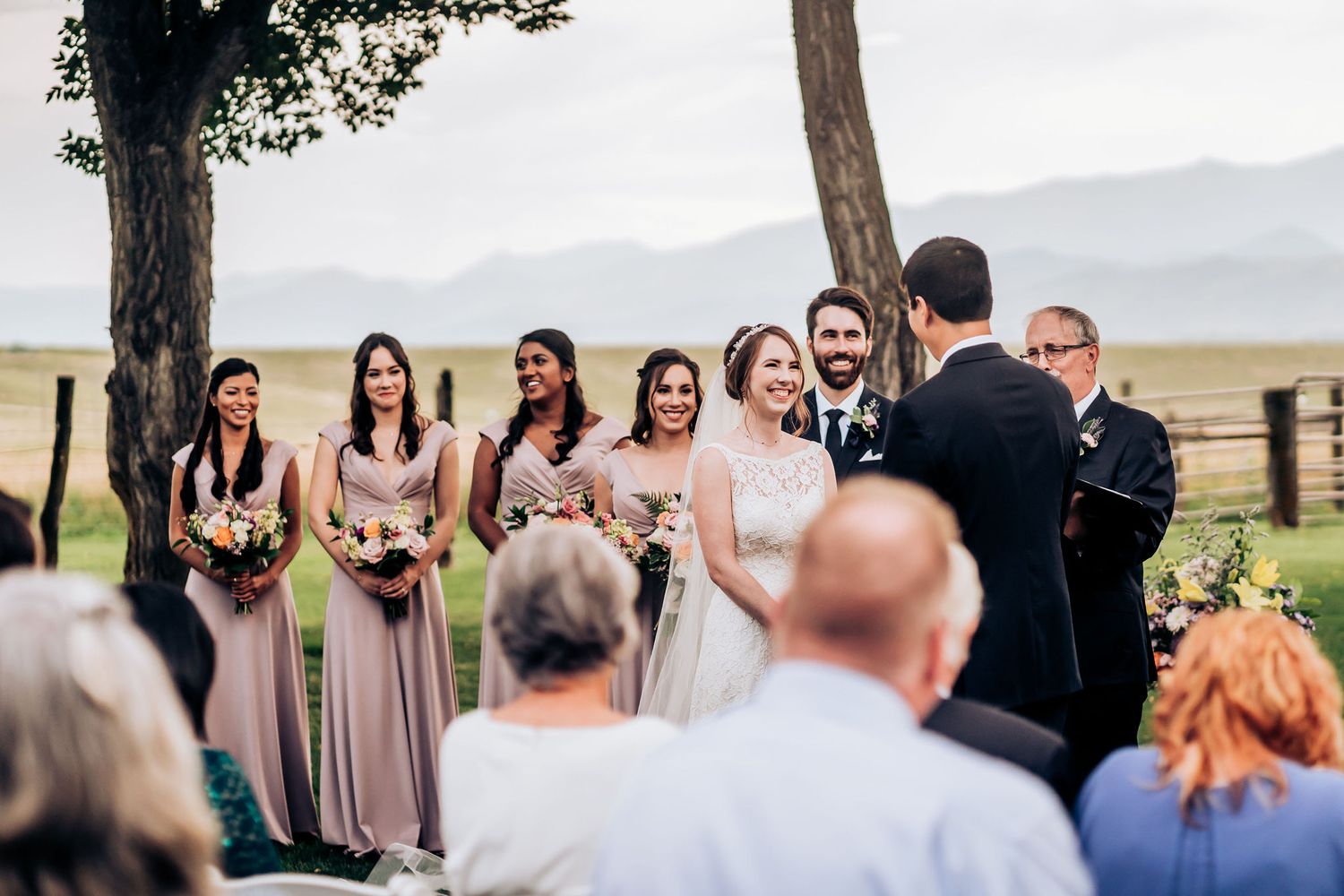 Scenic outdoor wedding ceremony with bridesmaids in blush dresses against mountain backdrop.
