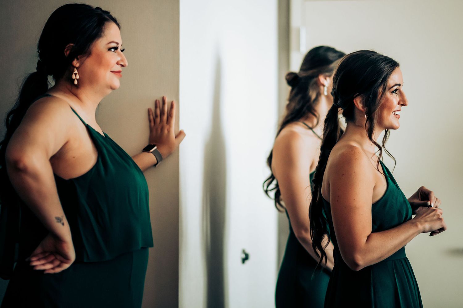 Bridesmaids in emerald green dresses getting ready in a naturally lit room.
