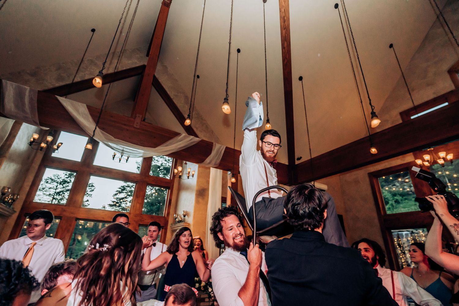 Festive wedding reception with guests lifting celebrants during an energetic dance party.