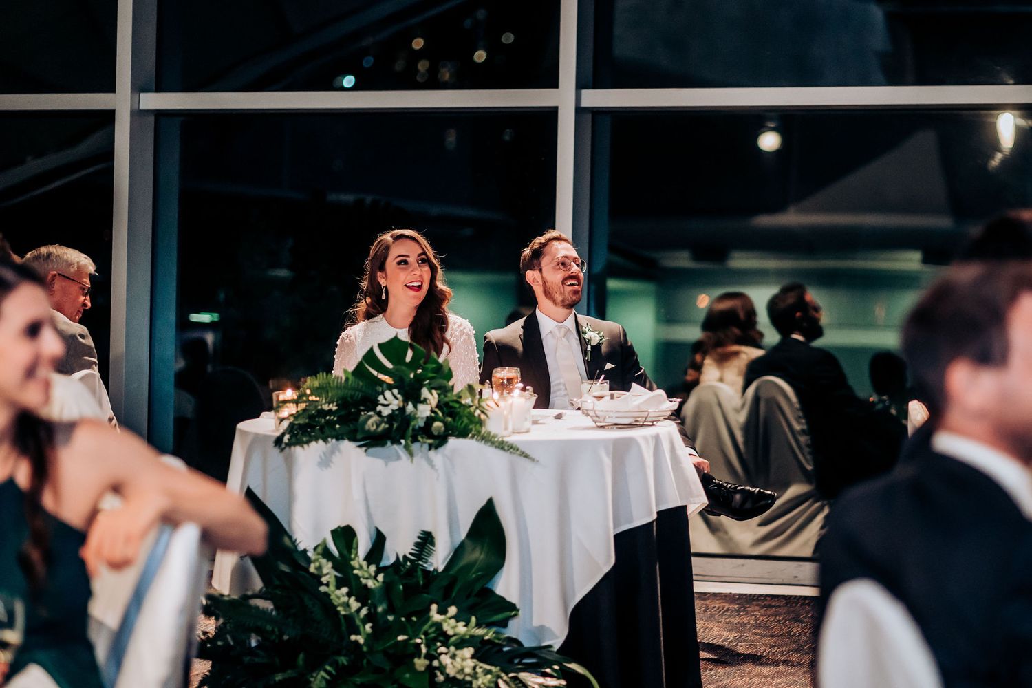 Wedding reception table setup with greenery decorations and elegant white tablecloths.