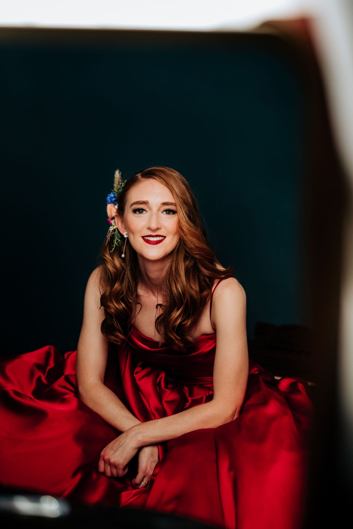 A figure in an elegant red satin gown poses gracefully against a dark background.