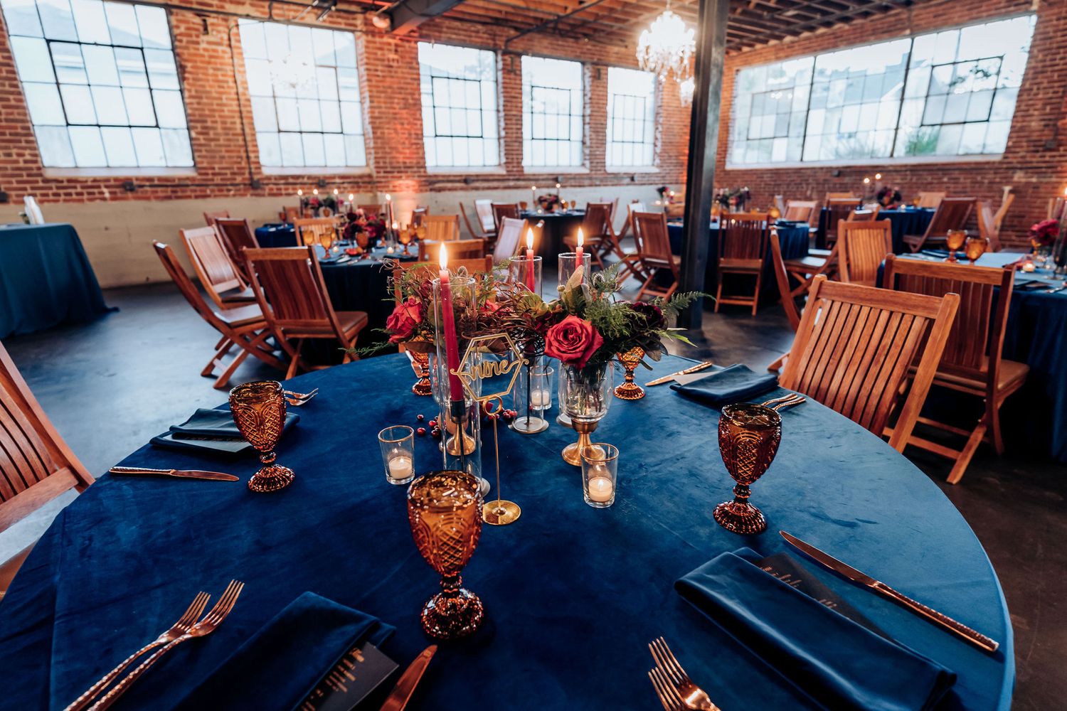Wedding reception table set with navy linens and gold accents in industrial brick venue.