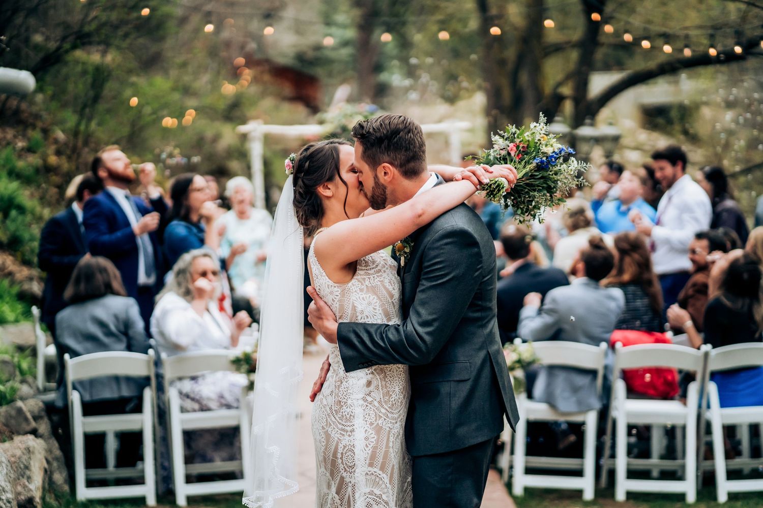 Wedding ceremony setup with string lights and mountain backdrop as guests look on.