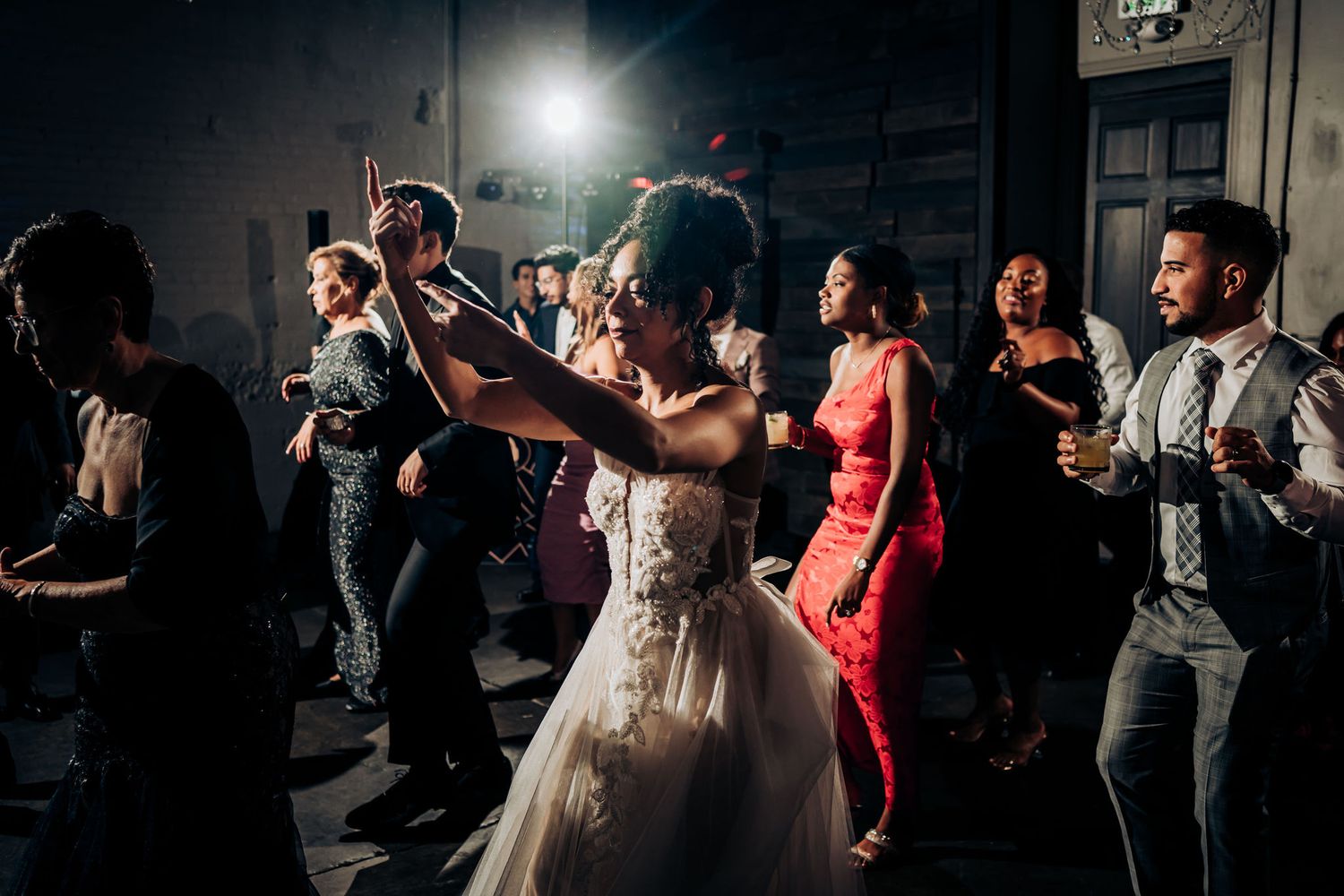Wedding reception dance party with guests dancing together under dramatic lighting.