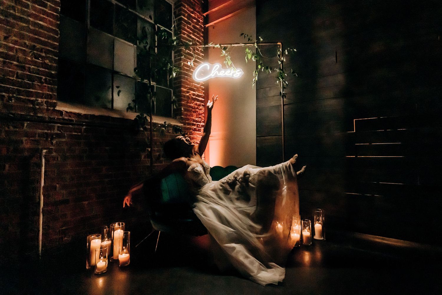 Dramatic wedding photo with couple in front of exposed brick wall illuminated by candles and neon light.