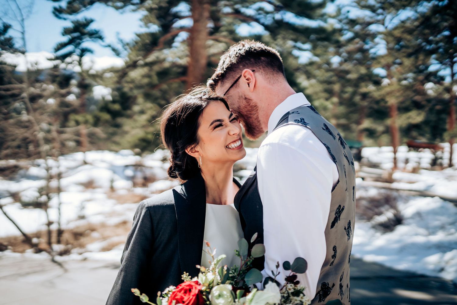 Intimate wedding portrait in a snow-covered mountain landscape with evergreen trees and winter florals.