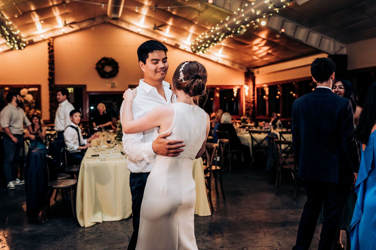 Couple embraces while dancing in an elegantly decorated reception venue with string lights.