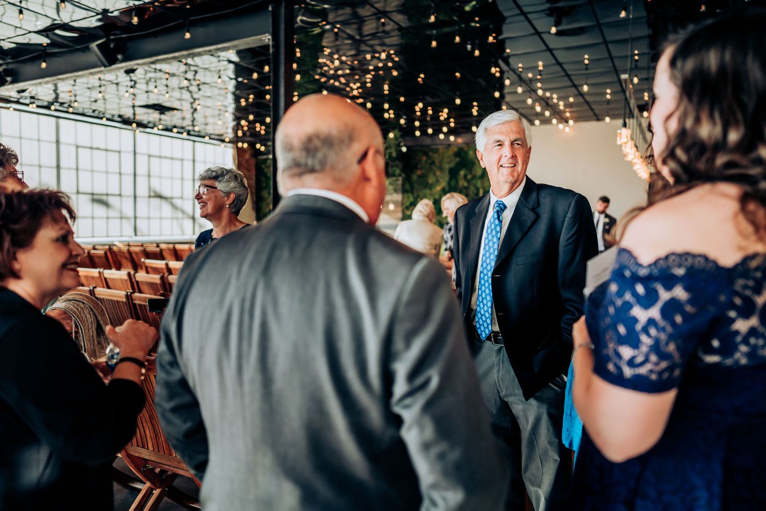 Guests gather at an indoor wedding reception venue decorated with string lights and modern decor.