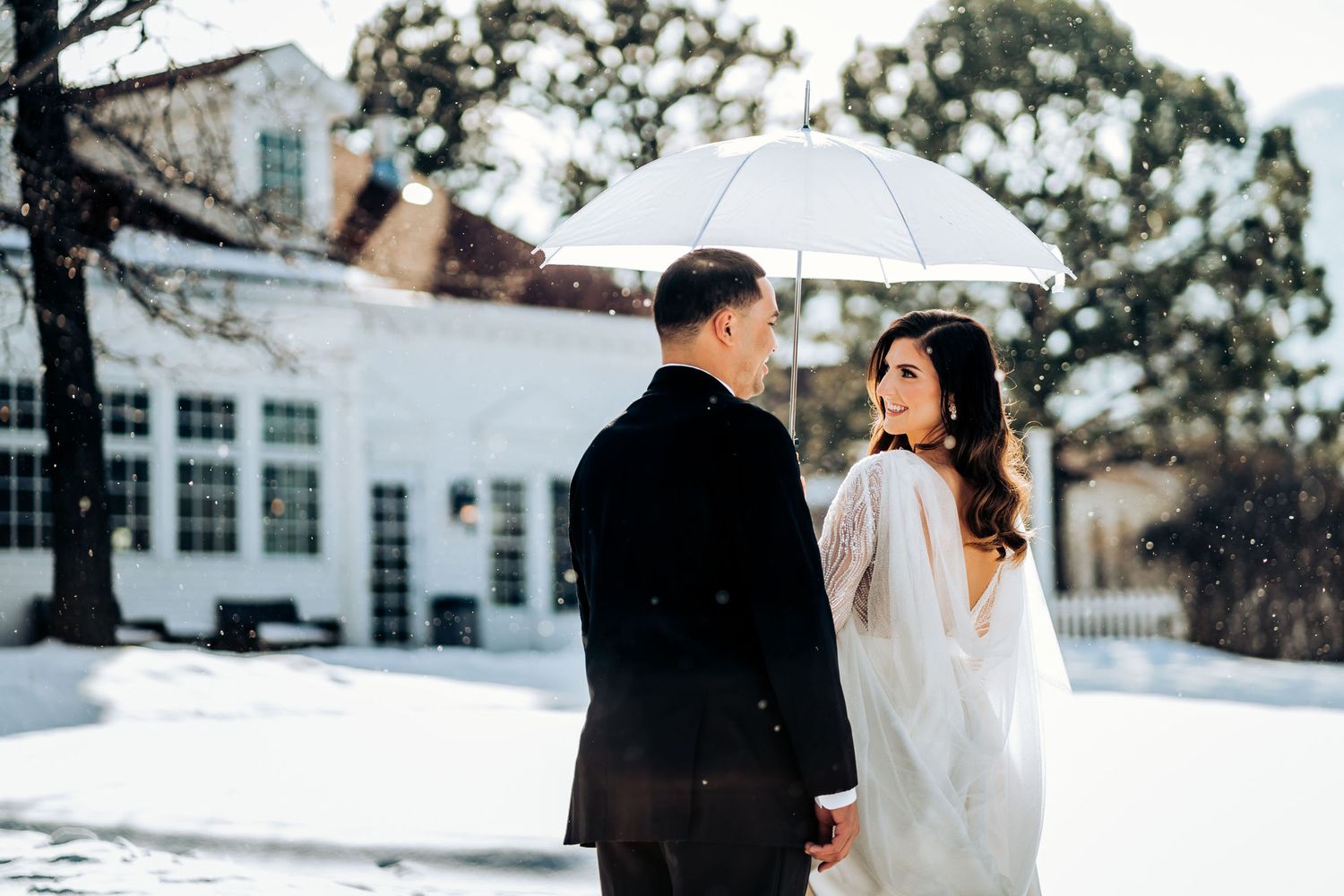 Romantic winter wedding portrait with couple sharing umbrella in the snow.
