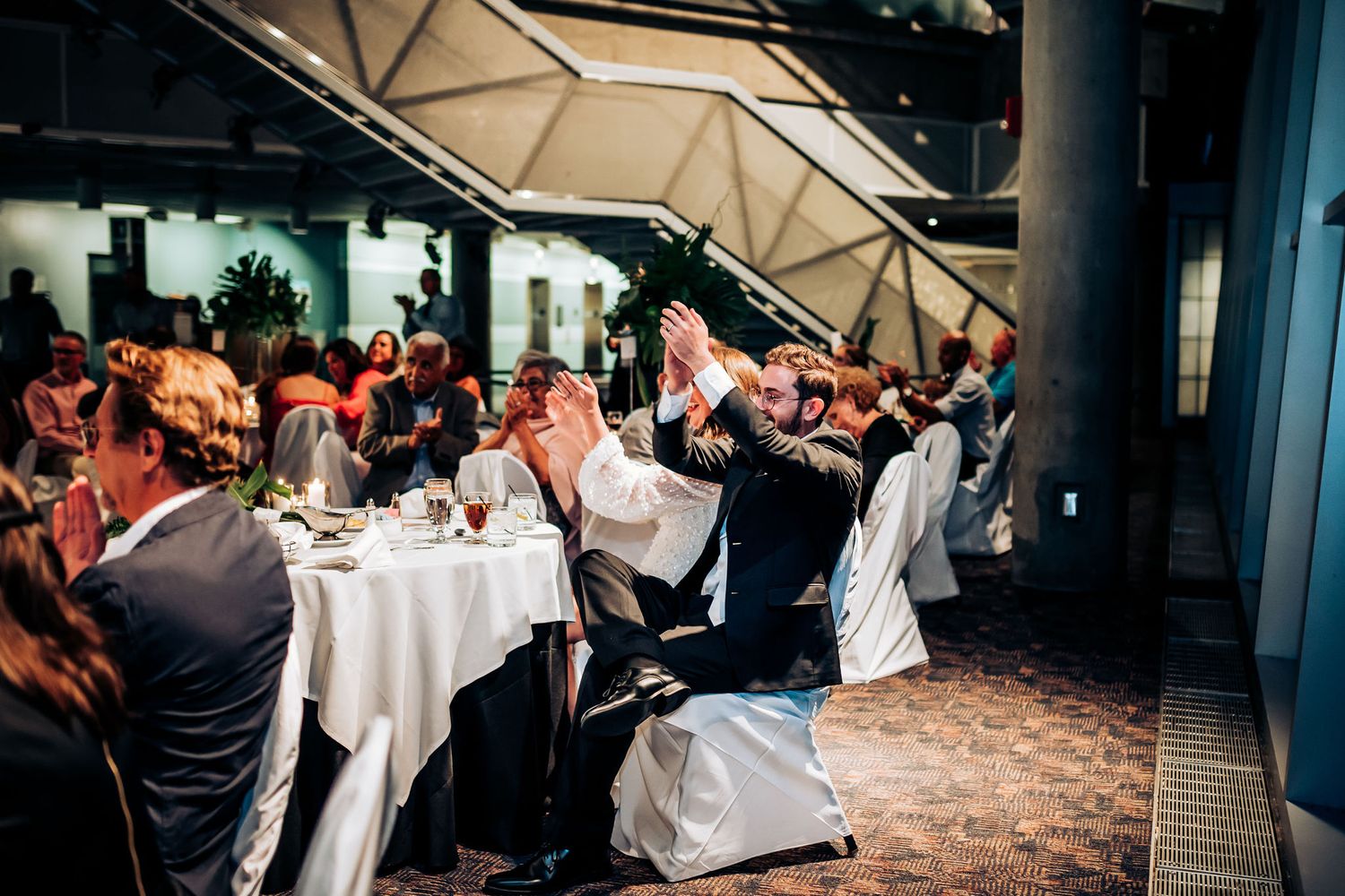 Wedding reception guests seated at decorated tables in modern venue space.