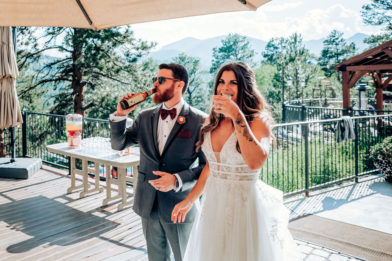 Newlyweds sharing drinks together on sunny outdoor terrace at mountain venue.