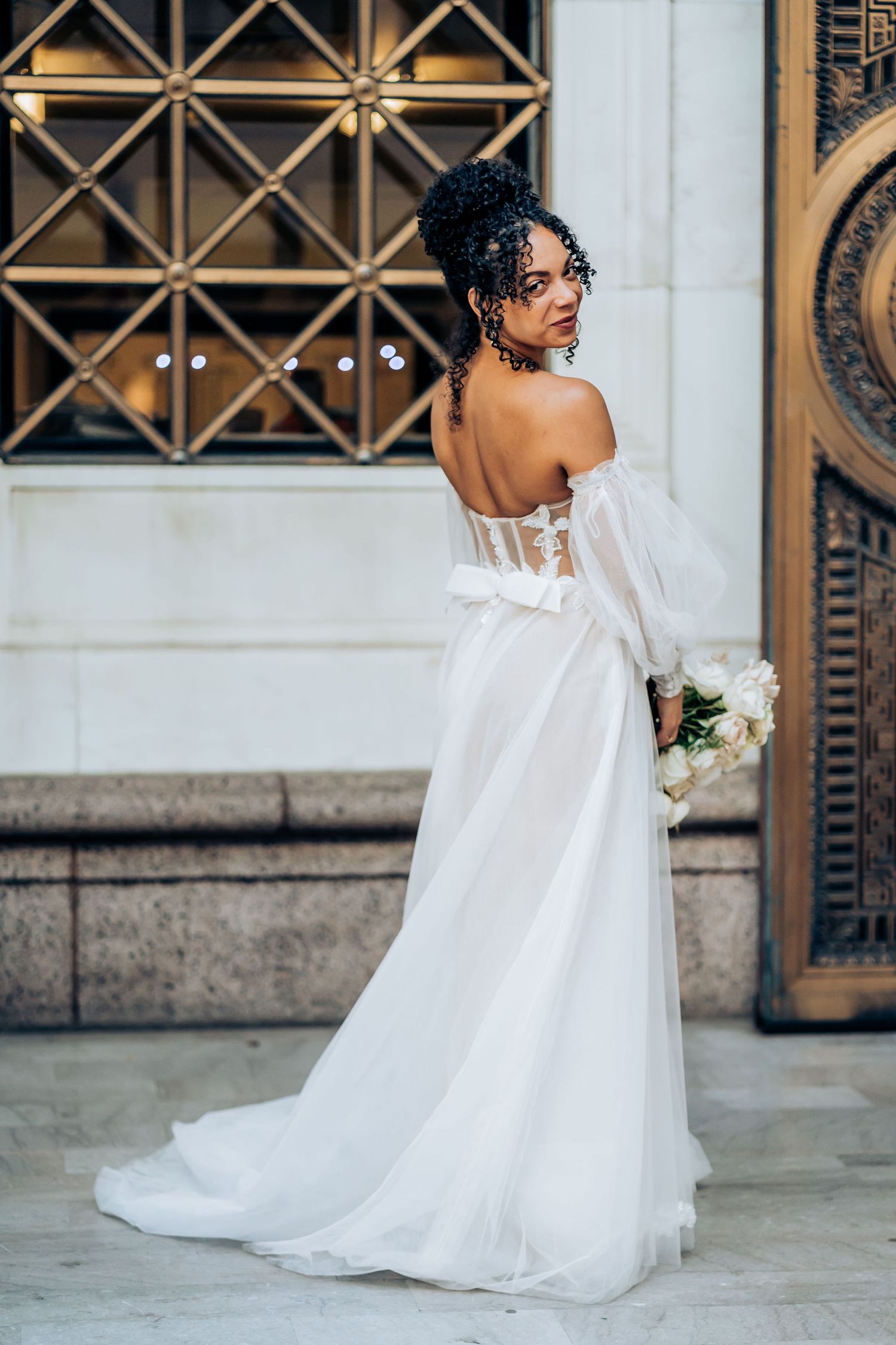 An elegant bridal portrait showing the back detail of a white off-shoulder wedding gown.