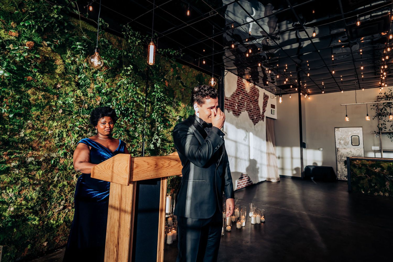 Emotional moment during wedding ceremony with indoor greenery and pendant lights.