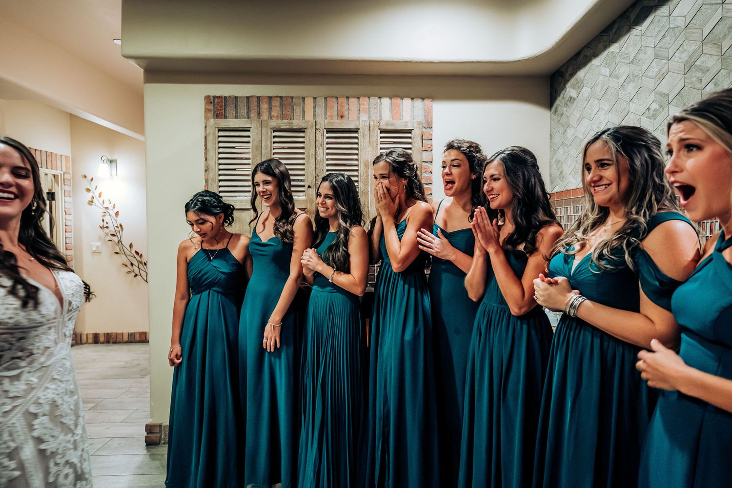 Wedding party in teal bridesmaid dresses reacting with excitement in a dressing room.