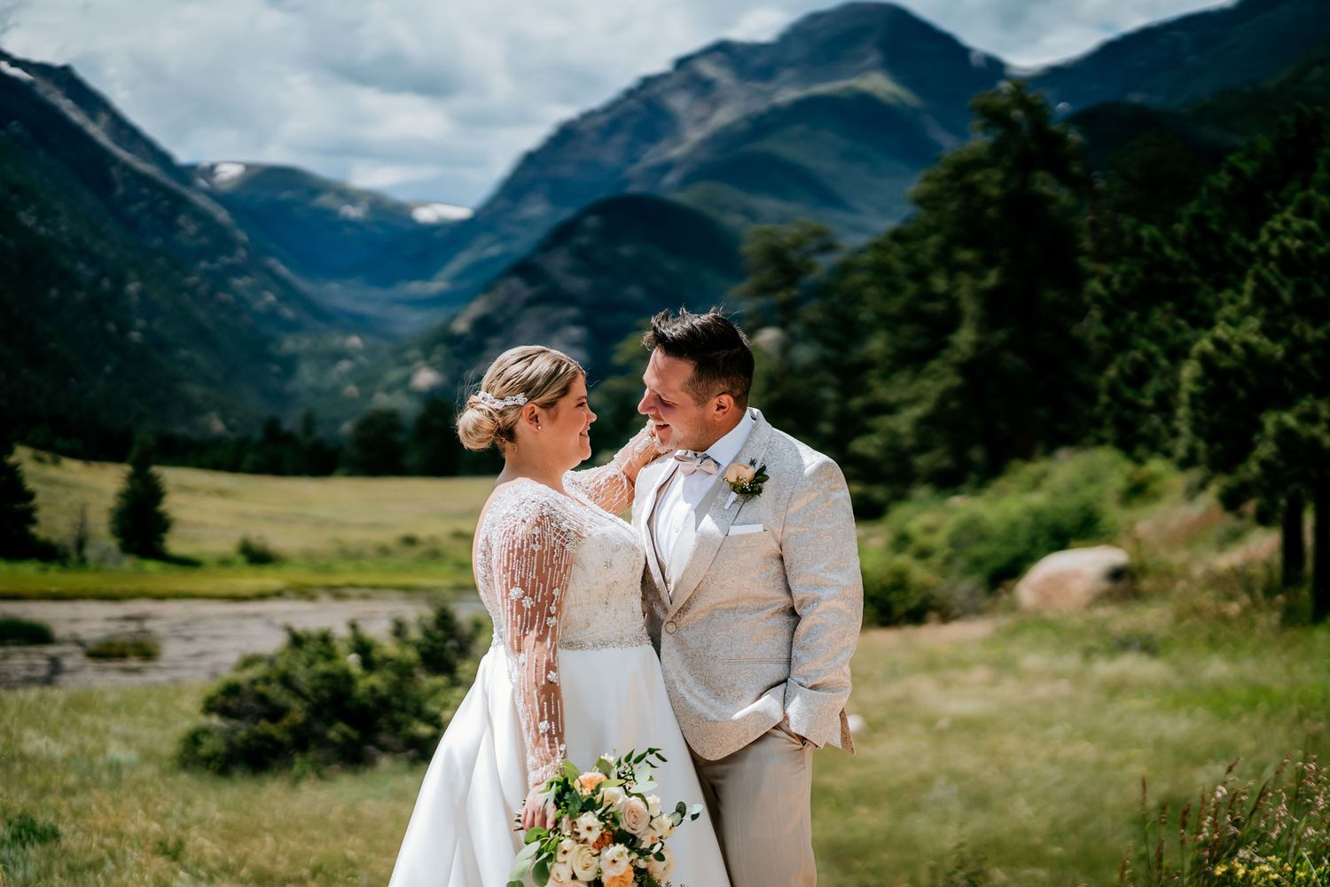 Newlyweds share an intimate moment in a scenic mountain valley with dramatic clouds overhead.