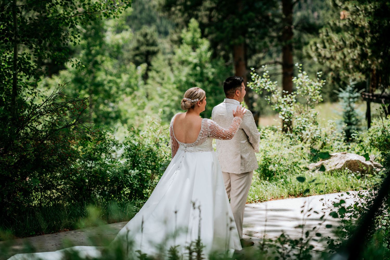 A couple in wedding attire walks along a garden path surrounded by lush greenery on their special day.