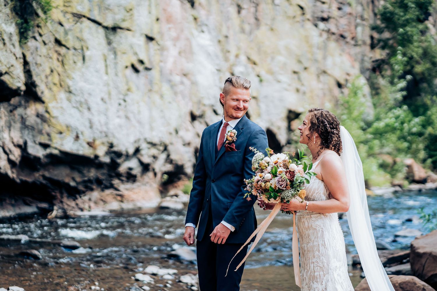 Joyful wedding moment captured by a scenic river with dramatic cliff backdrop.