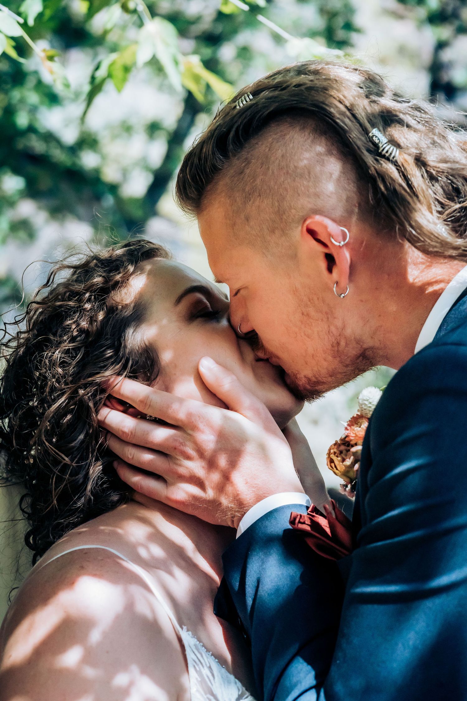 An intimate wedding portrait captures tender moment between newlyweds in natural outdoor setting.