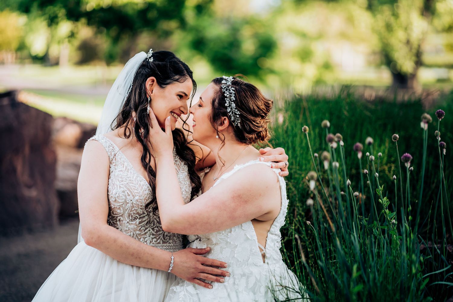 Joyful brides share a tender moment in a garden setting wearing matching white gowns.