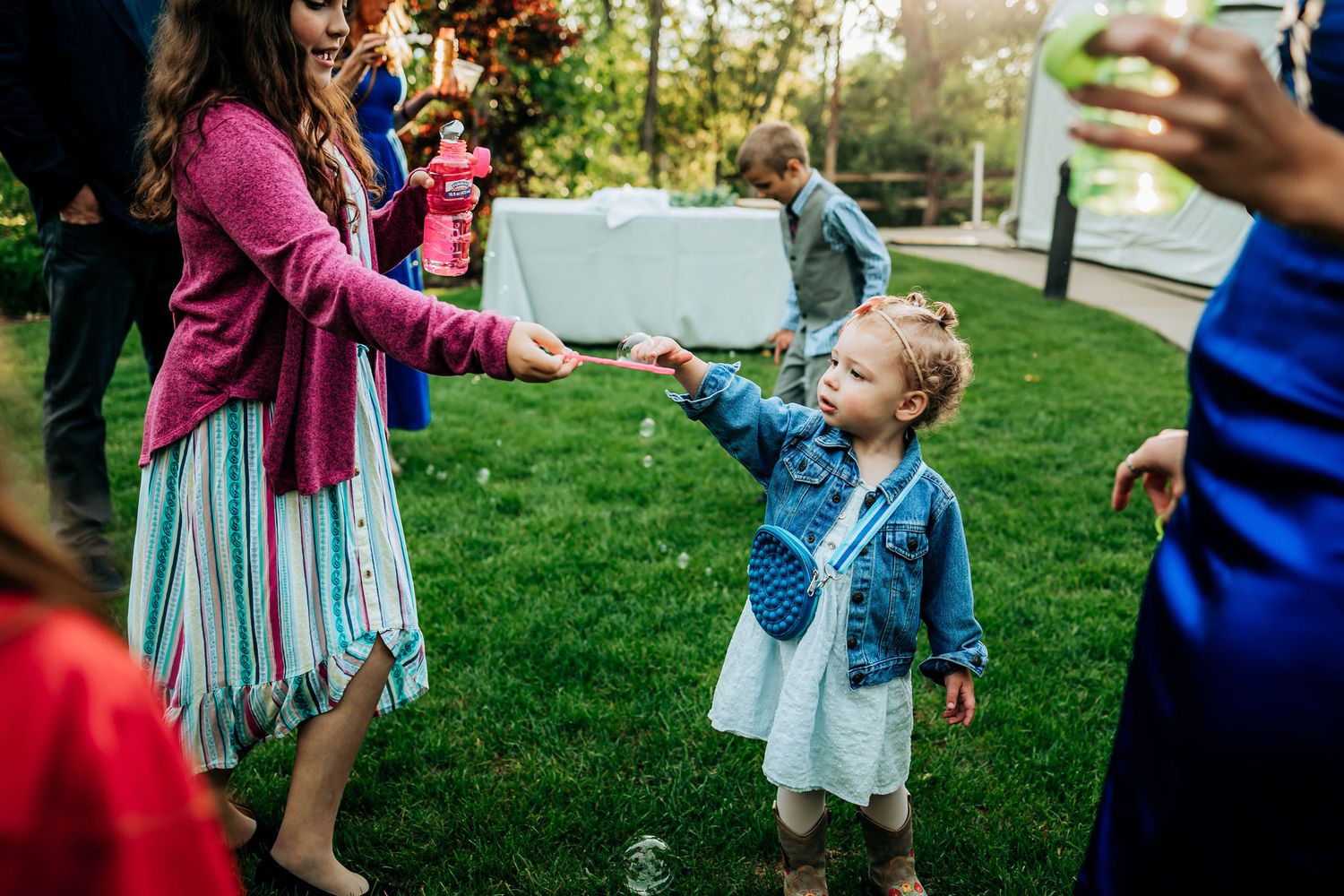 Kid in denim jacket plays with bubbles during outdoor celebration.