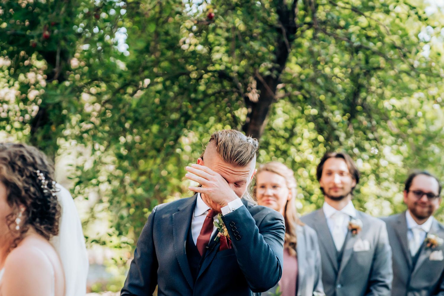 Emotional moment captured during outdoor wedding ceremony with wedding party in formal attire.