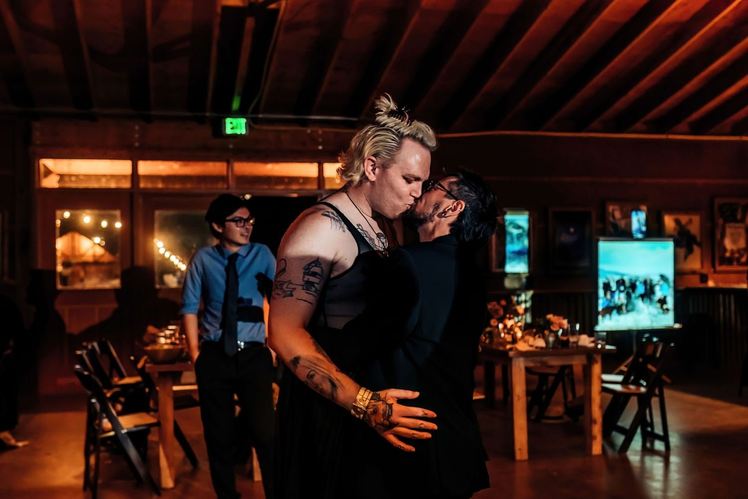 Couple dancing together in a dimly lit rustic venue with wooden beams overhead.