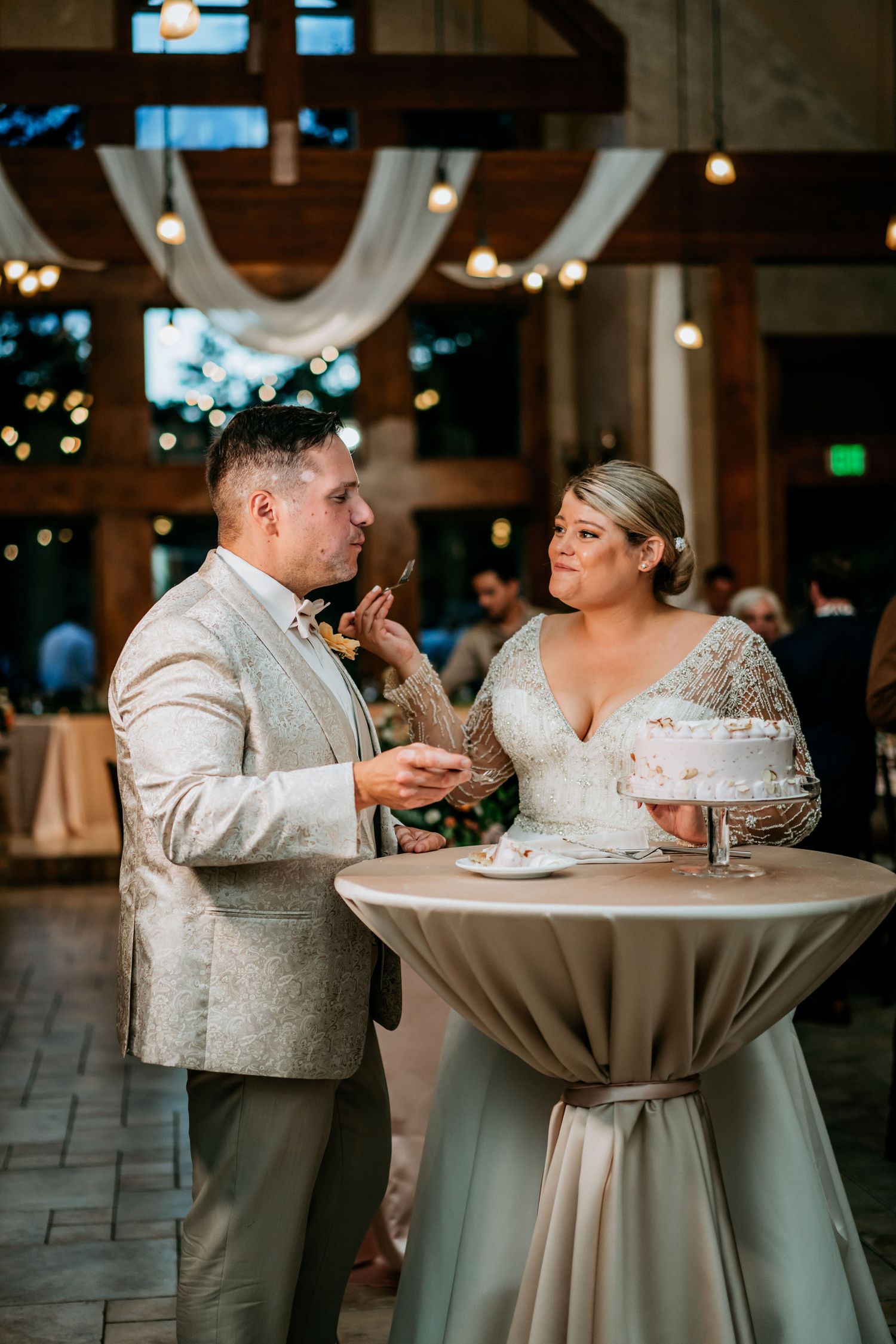 A couple shares their wedding cake at an elegant indoor reception venue decorated with white draping.