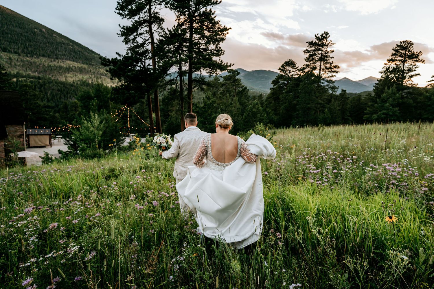 Bride walking through a wildflower meadow with mountain views at sunset.