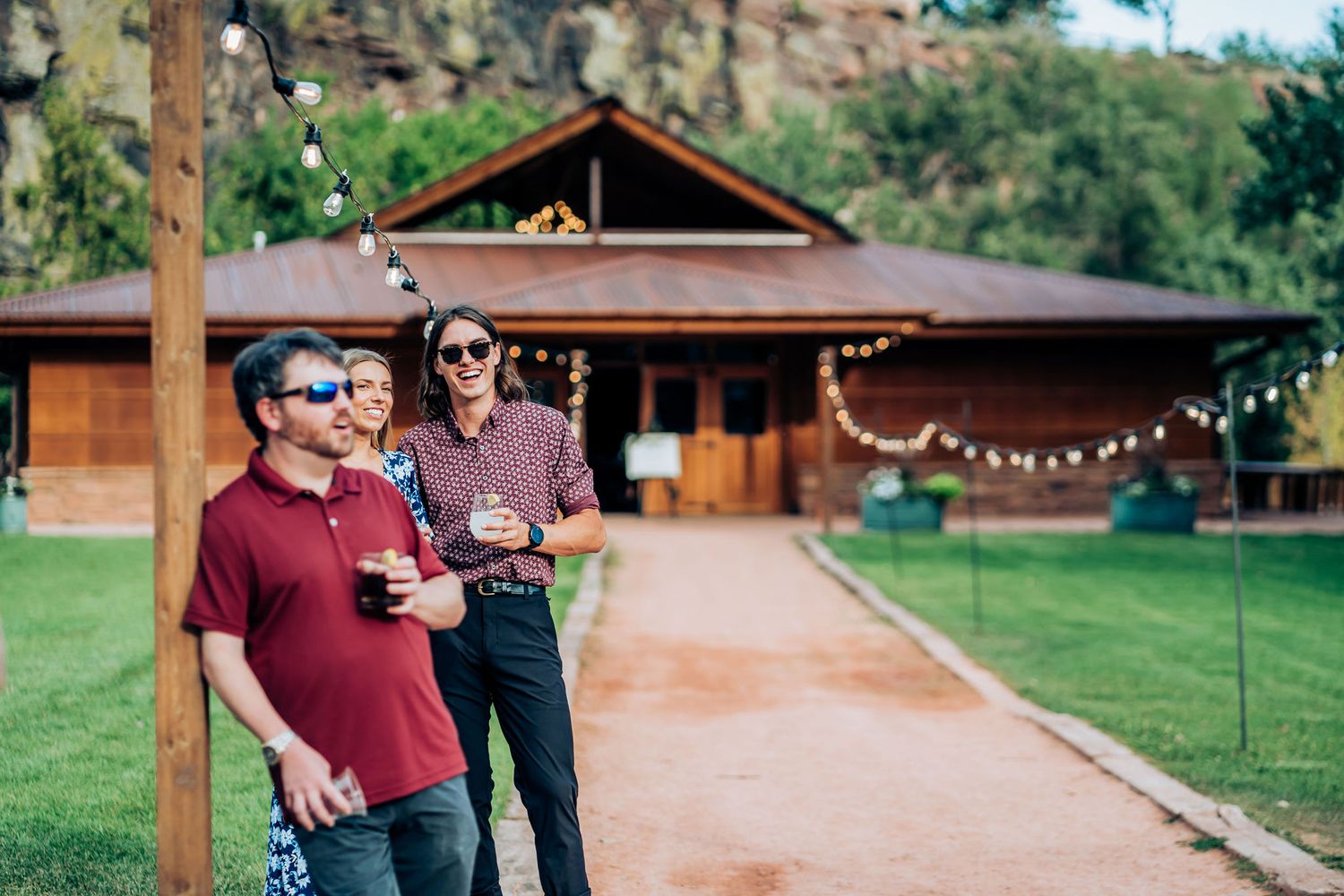 Rustic wood cabin with string lights sits beneath towering red rock formations.