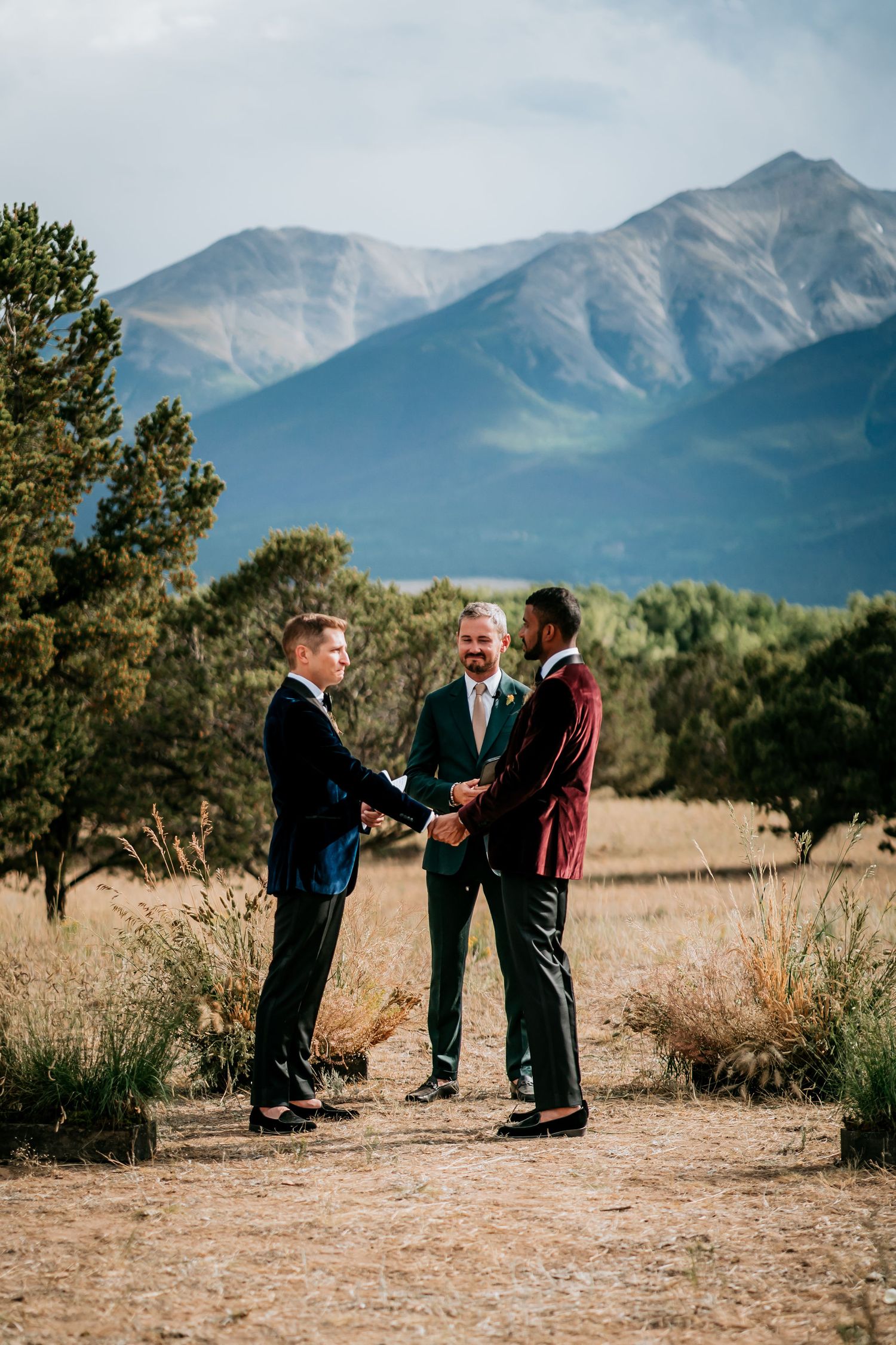 Three people participating in an intimate wedding ceremony with snow-capped mountains in the background.