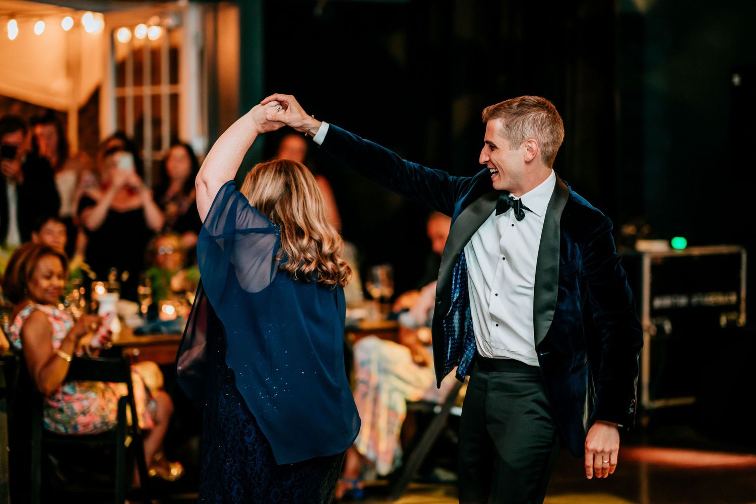 Dancing couple twirling on the dance floor at an elegant wedding reception while guests watch from their tables.
