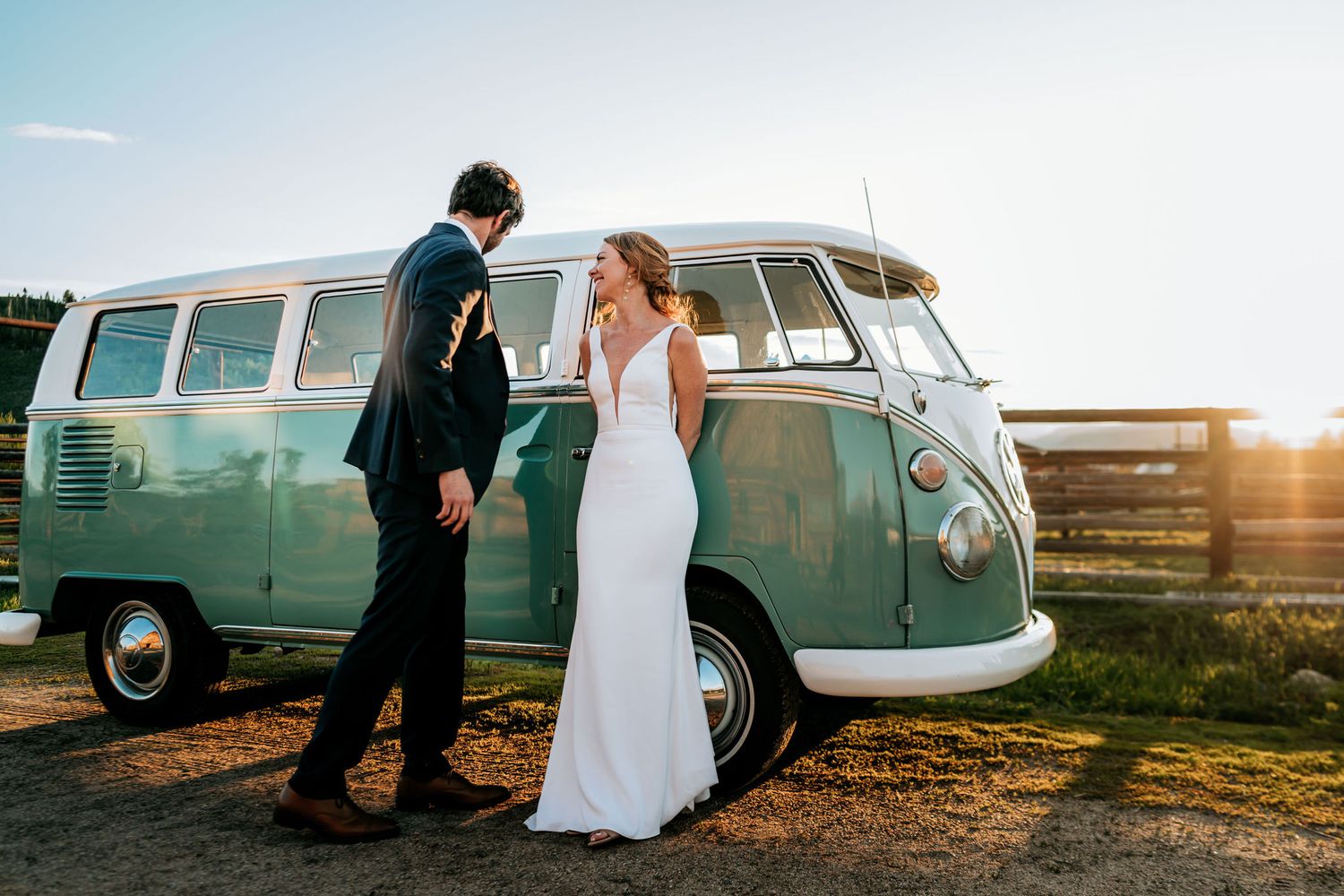 A wedding couple shares an intimate moment beside a vintage teal Volkswagen bus at sunset.