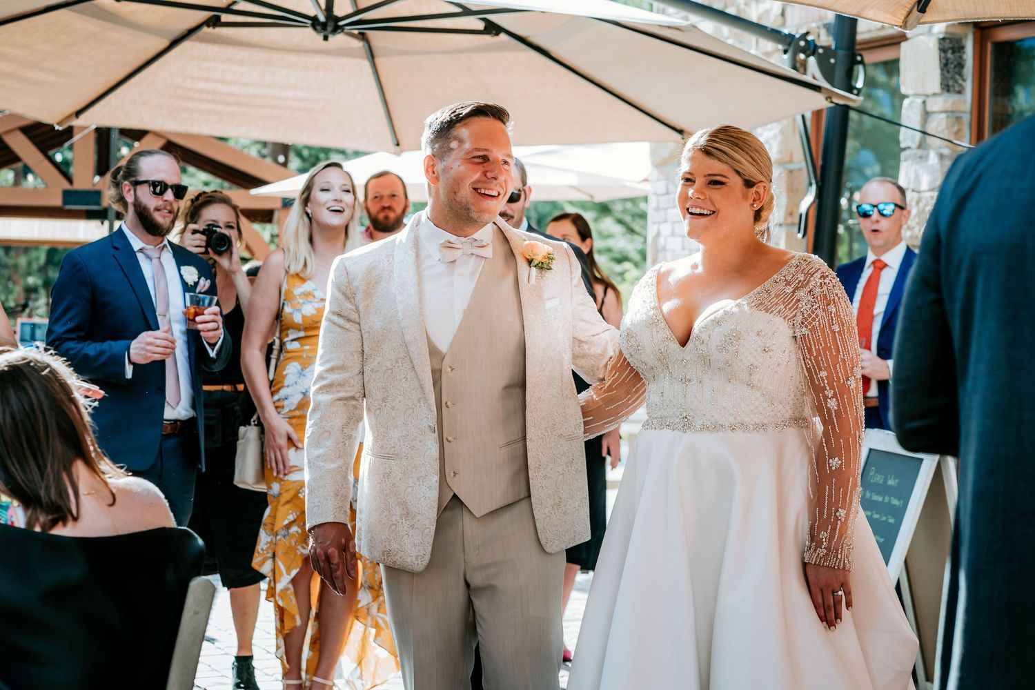 Wedding celebration under white umbrella with guests enjoying outdoor reception.