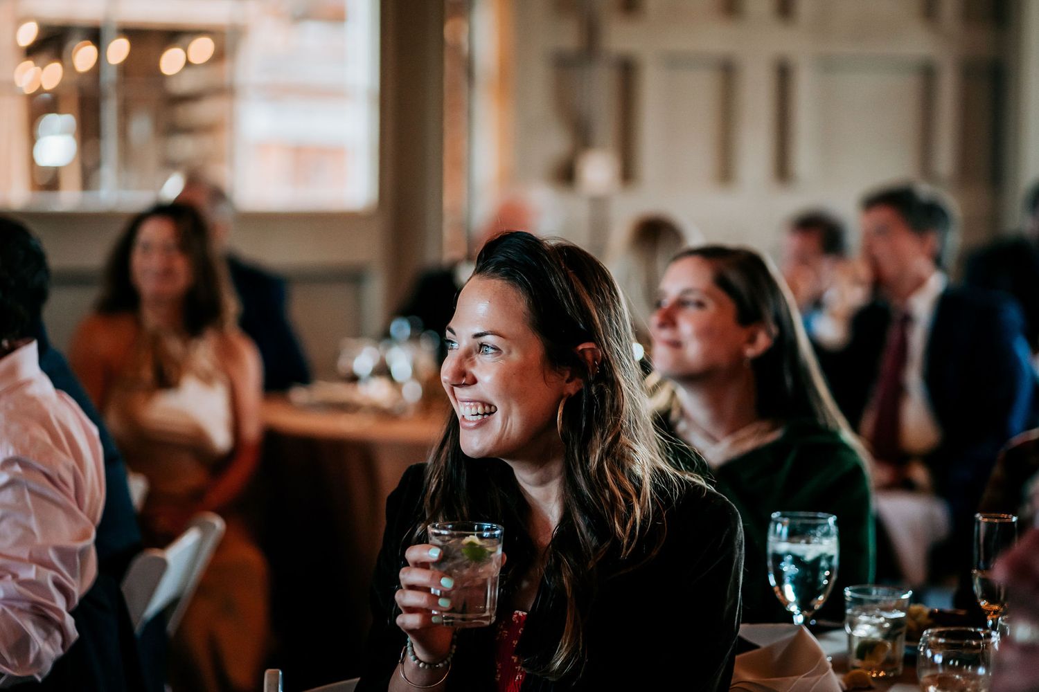 Guest smiles while enjoying drinks at wedding reception with warm lighting.